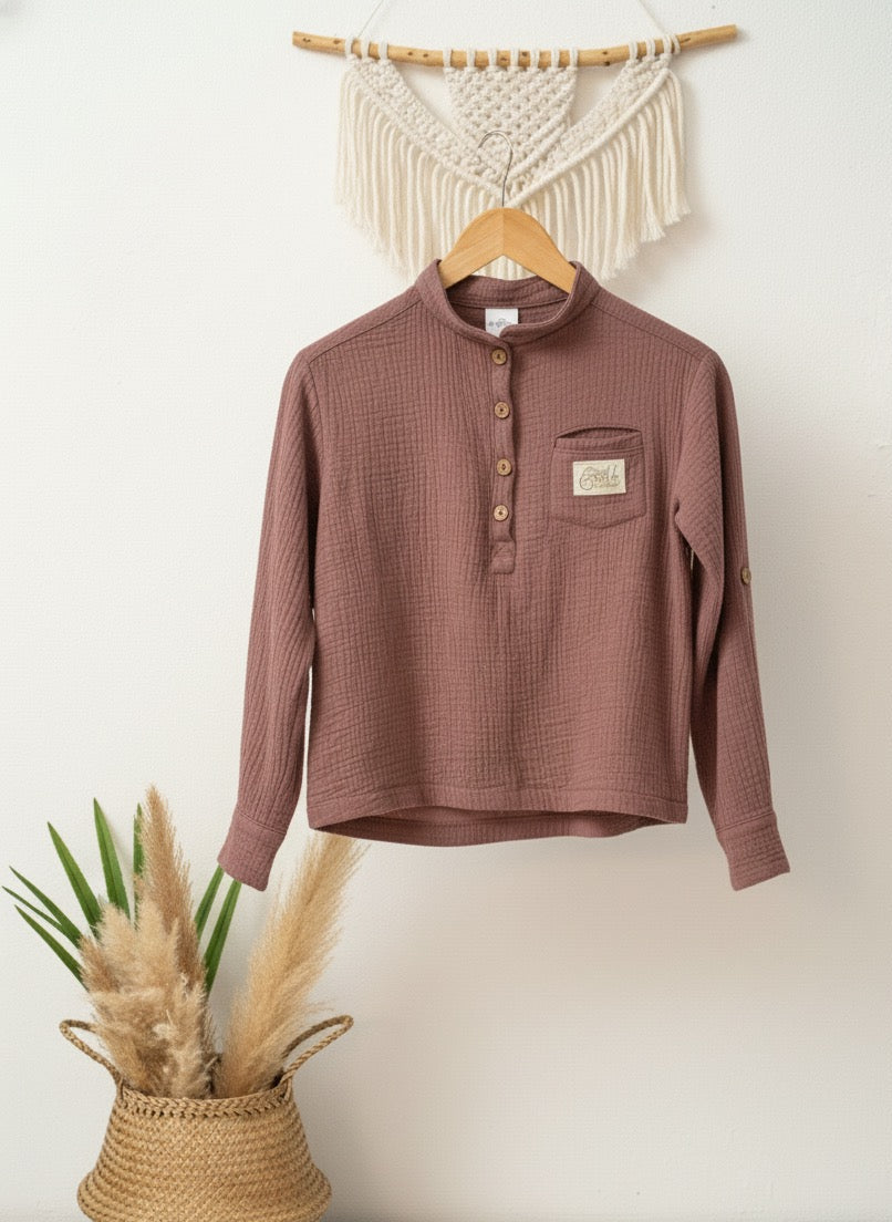 Mauve farbenes Musselinhemd mit Reverskragen an einer weißen Wand aufgehängt an einem Makramee