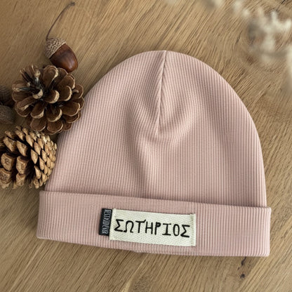 Gerippte Beanie Mütze mit Namen auf weißem Label und shcwarzen Weblabel "Best Kind ever" auf eineem Eicheholztisch daneben Tannenzapfen und Eicheln. Farbe der Mütze: Altrosa.