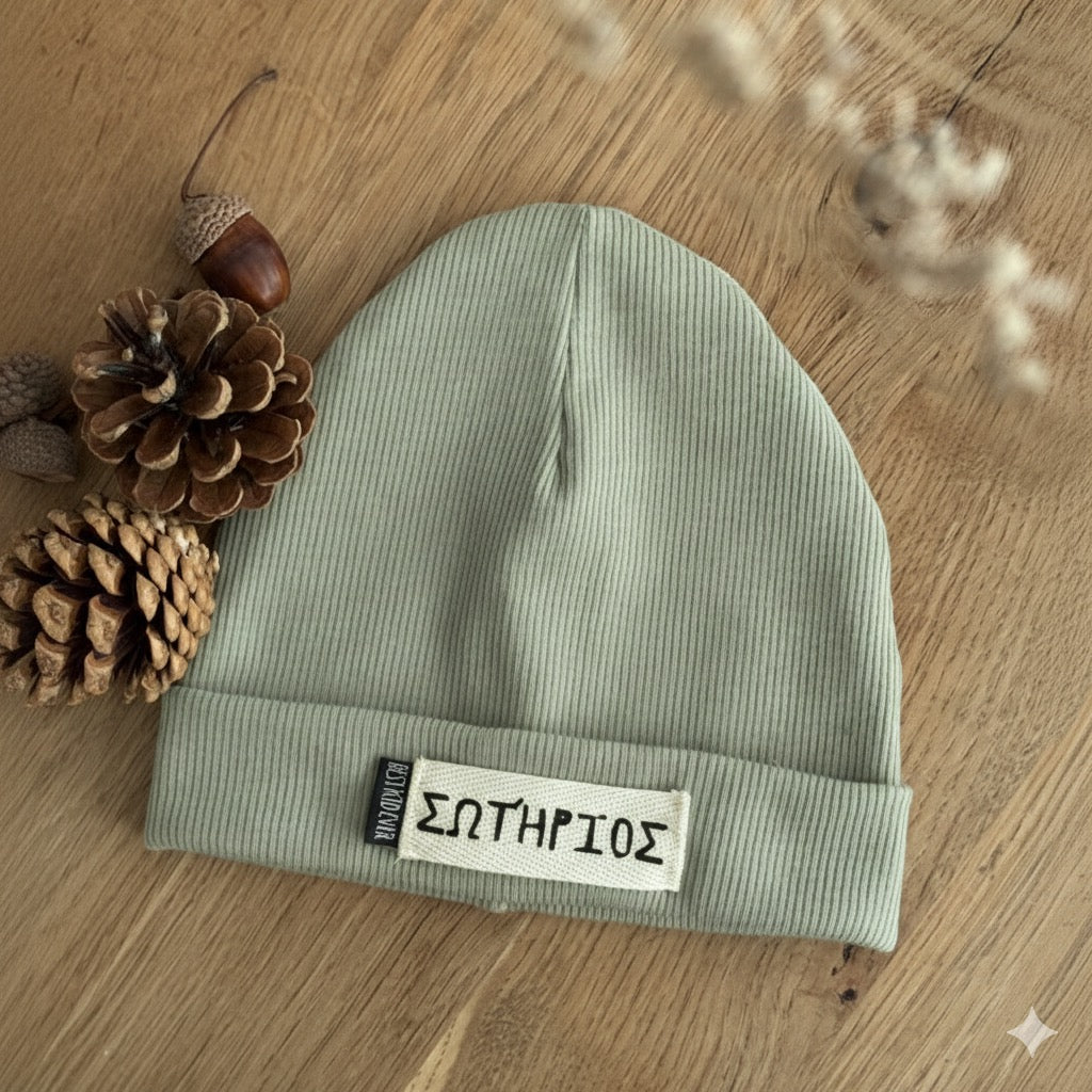 Gerippte Beanie Mütze mit Namen auf weißem Label und shcwarzen Weblabel "Best Kind ever" auf eineem Eicheholztisch daneben Tannenzapfen und Eicheln. Farbe der Mütze: Mint.